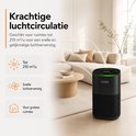 Zwarte luchtreiniger met groen verlicht display, in een ruime woonkamer. Krachtige luchtcirculatie tot 210 m³/u.