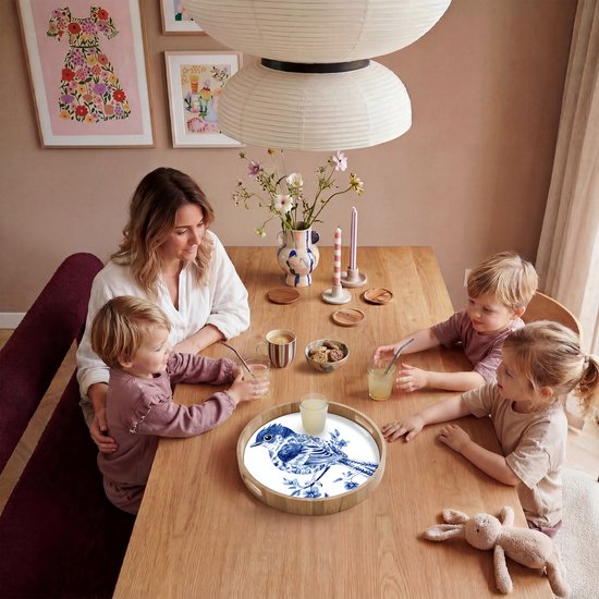 Rond houten dienblad met Delfts blauw vogeldecor, op een eettafel met een gezin.