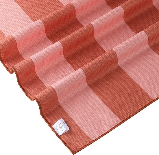 Deken met verticale banen in koraalroze en lichter roze. De stof heeft een wafelstructuur. Een label met een zon en 'Piece of Sun' is zichtbaar.