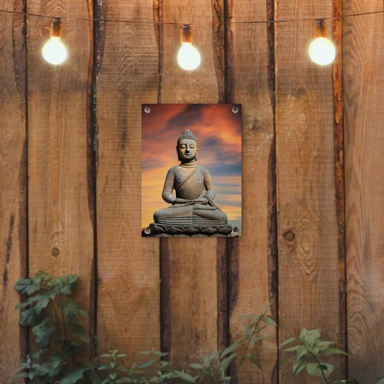 Bouddha en pierre sur une fleur de lotus sur fond de coucher de soleil, suspendu à une clôture en bois avec des guirlandes lumineuses.