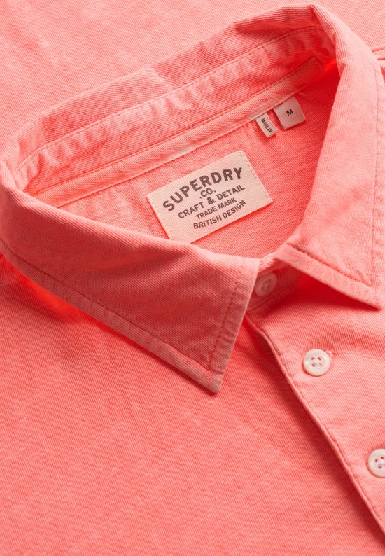 Close-up van de kraag van een oranje Superdry poloshirt met waslabel.