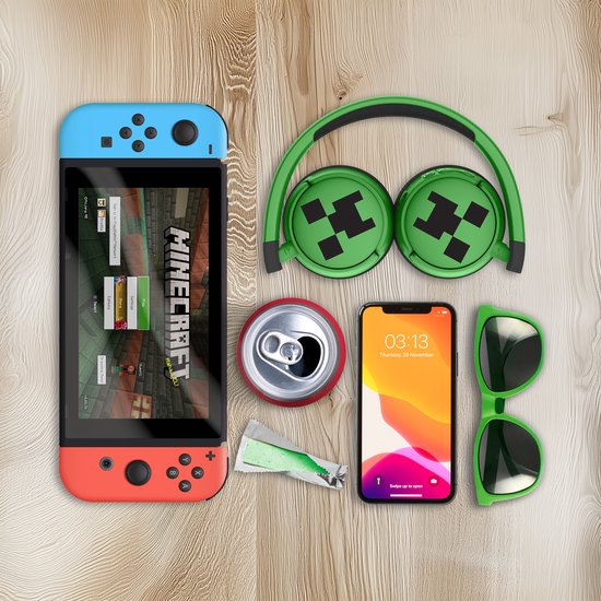 Groene Minecraft draadloze koptelefoon met Creeper-print, naast een Nintendo Switch, smartphone en zonnebril.