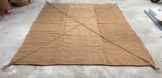 Bruin kokosvezel schaduwdoek, 5x5 meter, op betonnen vloer, met kruislings lopende stiksels en metalen oogjes.