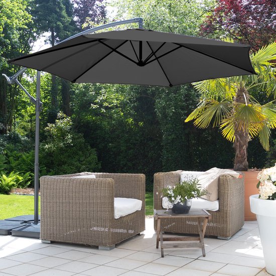 Grijze zweefparasol staat boven twee rieten stoelen op een terras met een palmbomen.