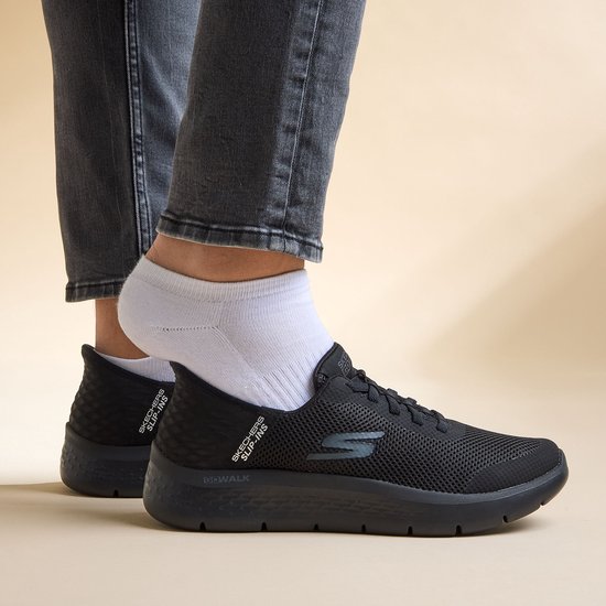 Zwarte Skechers Go Walk Flex instappers met grijs logo en 'Slip-Ins' opdruk, gedragen met grijze jeans.