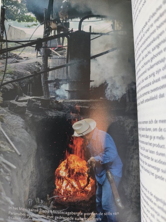 Man in hoed met blauwe blouse stookt vuur onder een destilleerketel in een Mexicaanse stookplaats.