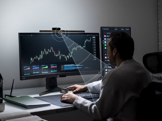 Man die naar een computerkabel kijkt met de BenQ ScreenBar Halo erop gemonteerd, met lichtstralen die het scherm verlichten.