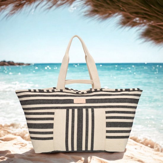 Beige strandtas met zwart gestreepte patronen op een strand met de zee op de achtergrond.