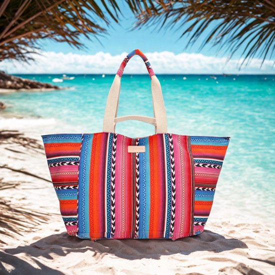 Grote tas met kleurrijke strepen in fuchsia, oranje, blauw en zwart. Beige hengsels. Strandachtergrond.
