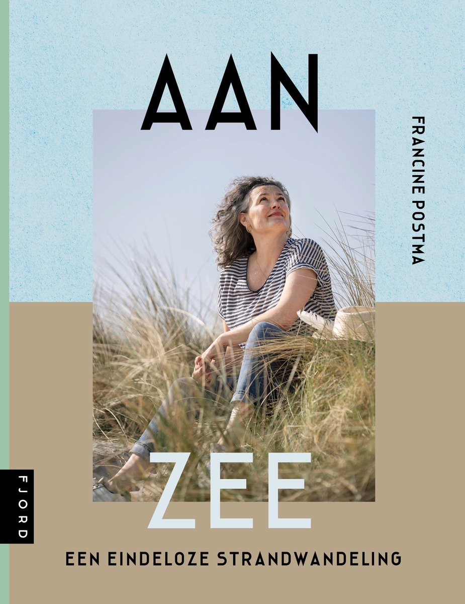 Vrouw met grijze krullen, zittend in het gras, met gestreepte top en spijkerbroek. Boek "Aan Zee".