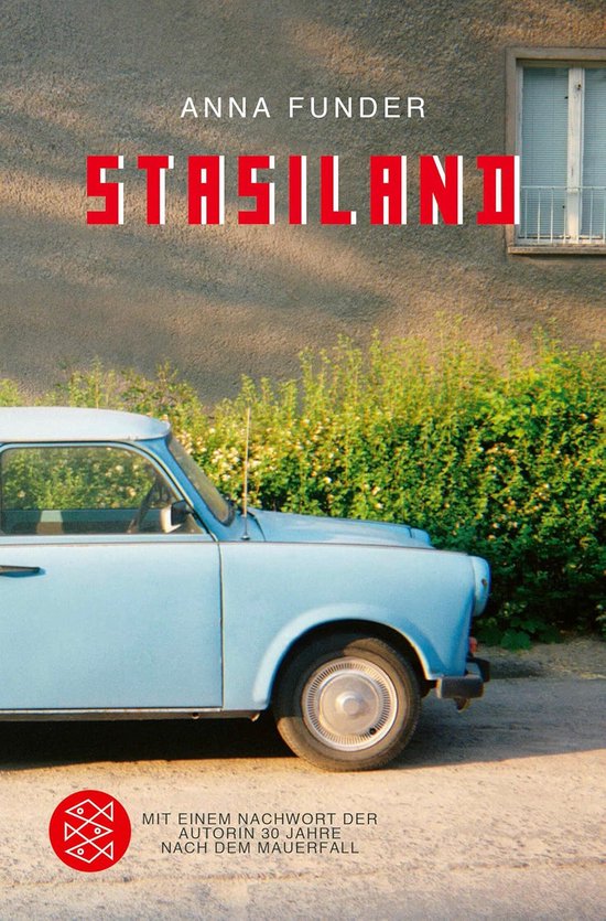 Boek 'Stasiland' van Anna Funder, met rode letters op een grijze muur. Een blauwe Trabant staat ervoor.