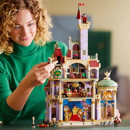 Vrouw in groene coltrui bouwt aan het LEGO Disney Belle en het Beest Kasteel.