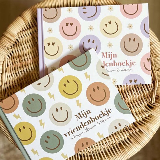 Twee vriendenboekjes op een mandje, beide met een patroon van lachende gezichten en bloemen.