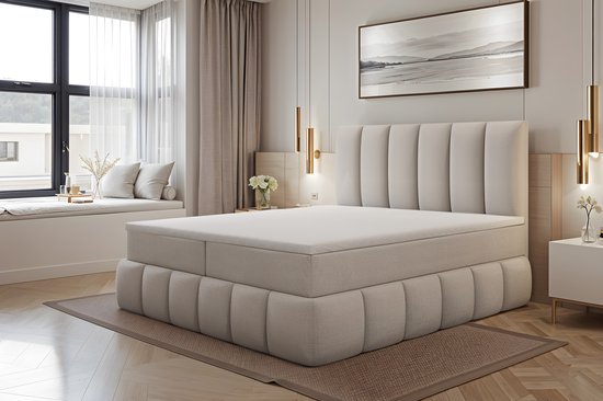 Beige boxspring met gestoffeerde basis en hoofdbord in een slaapkamerinterieur, inclusief topper.