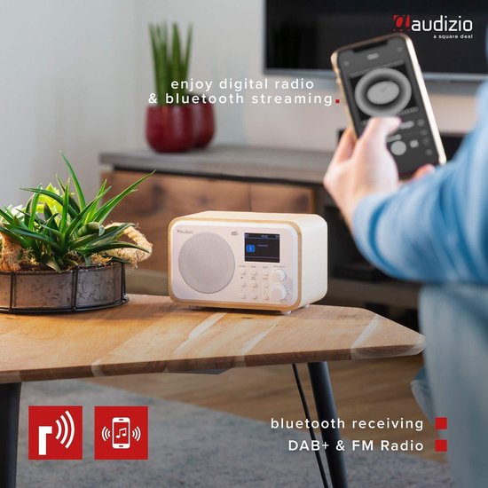 DAB radio met wit front en houten kast op een salontafel, met een telefoon in de buurt.