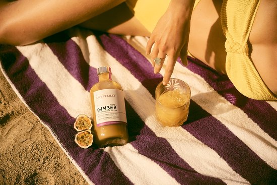 Een fles GIMBER en een glas met GIMBER op een gestreepte handdoek op het strand.