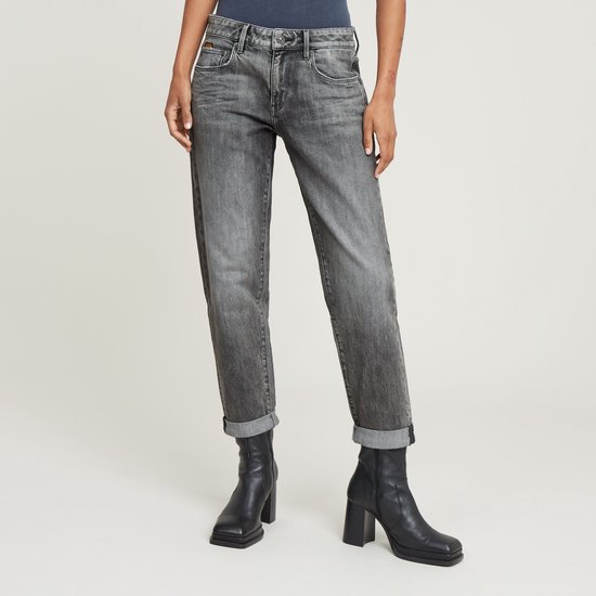 Vrouw in grijze G-Star jeans met opgerolde broekspijpen, zwarte enkellaarzen en donkerblauwe top.