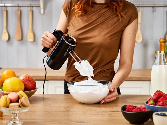 Vrouw met rode haren in een bruine trui mixt schuim met een zwarte Lafe handmixer.