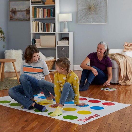 Een vrouw en twee kinderen spelen Twister in een woonkamer. Ze zitten op de mat met rode, gele, blauwe en groene cirkels.