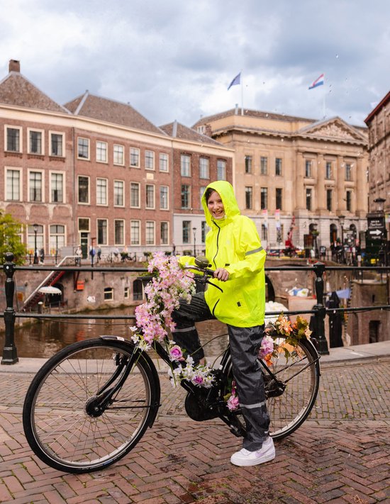 Jong meisje in fluoriserende gele regenjas en grijze regenbroek, staand op een fiets versierd met bloemen.