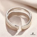 Zilverkleurige ring met drie parallelle, overlappende banden, op een zijden stof.