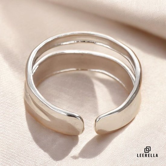Zilverkleurige ring met drie parallelle, overlappende banden, op een zijden stof.