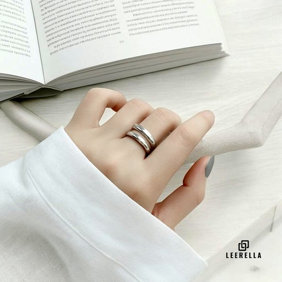 Vrouwshand draagt een zilverkleurige ring met twee gladde, overlappende banden aan de wijsvinger.