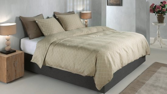 Opgemaakte tweepersoonsbed met beige dekbedovertrek met patroon, kussens en nachtkastjes met lampen, met bloemen op een bijzettafel.