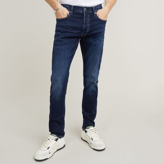 Man met donkerblauwe G-Star 3301 slim jeans met lichte wassing, gedragen met witte sneakers.