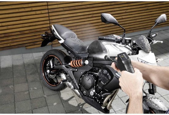 Hand met hogedrukreiniger spuitend op een motorfiets.