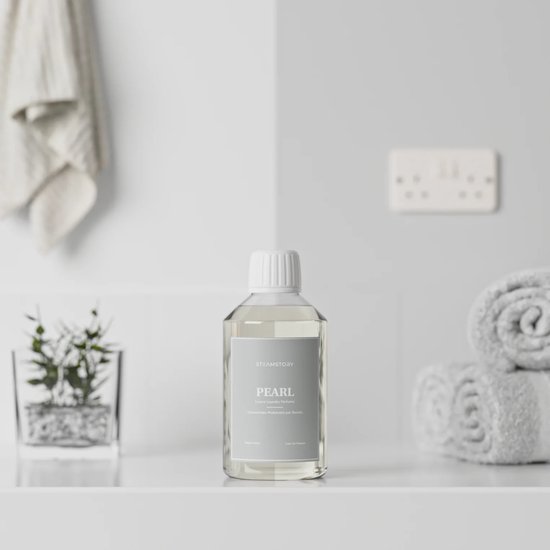 Fles Steamstory wasparfum 'Pearl' op een plank met handdoeken en een plant.
