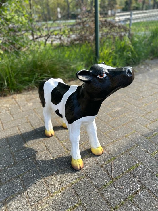 Statue de veau noir et blanc regarde vers le haut, avec des yeux marron, des pattes blanches et des sabots dorés.