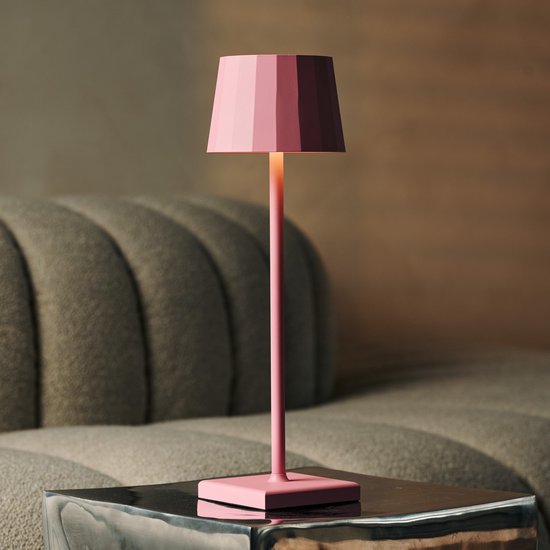 Lampe de table rose avec pied carré, légèrement éclairée, sur une table d'appoint.