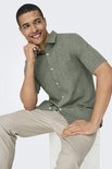 Man in een groen, kortarmig hemd met witte knopen en een beige broek.