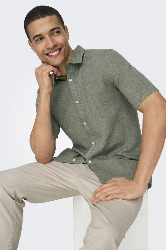 Man in een groen, kortarmig hemd met witte knopen en een beige broek.