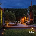 Een tuin in de avond, verlicht door Xelloo spots die warm licht geven op het gazon en de beplanting.