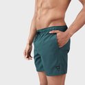 Homme de profil, portant un maillot de bain vert foncé avec cordon et logo sur la jambe.