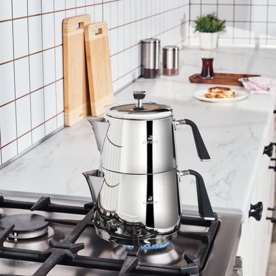 Zilverkleurige roestvrijstalen theepot met zwarte handvatten, bovenop een gasfornuis.