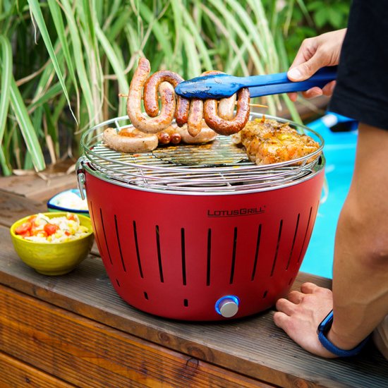 Rode LotusGrill met worstjes en kip, een persoon gebruikt een tang.