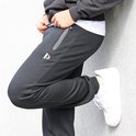 Zwarte joggingbroek voor heren, close-up van de zijkant met ritszak en witte sneaker.