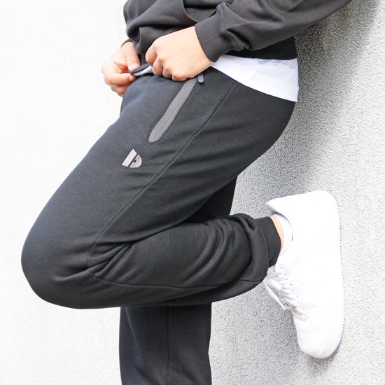 Zwarte joggingbroek voor heren, close-up van de zijkant met ritszak en witte sneaker.