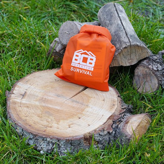 Oranje BCB Adventure Survival tasje met trekkoord, liggend op een boomstronk buiten.