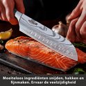 Een Nazrom keukenmes met damastpatroon snijdt moeiteloos in een stuk zalm, met knoflook en kruiden op de achtergrond.