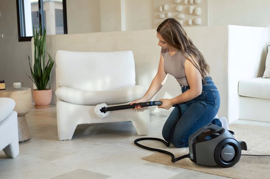 Une femme nettoie un fauteuil blanc avec un nettoyeur vapeur muni d'une brosse.