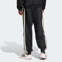 Achterkant van een man in zwarte trainingsbroek met witte strepen en Adidas logo, gedragen met witte sneakers.