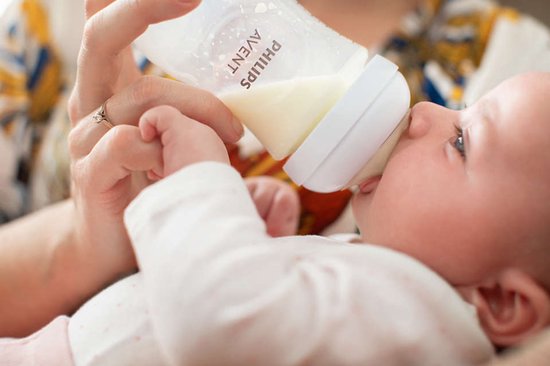 Een baby wordt gevoed met een Philips Avent babyfles door een persoon met een ring aan haar vinger.