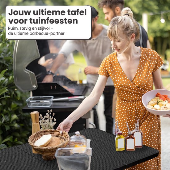 Zwarte tafel met rotan-look, met eten erop, bij een barbecue met mensen.