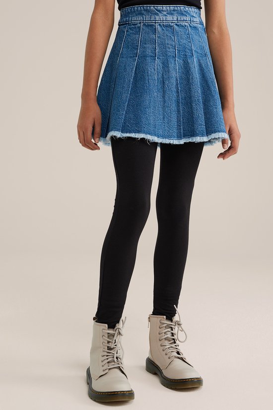 Een meisje met een spijkerrokje en zwarte legging.