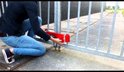 Persoon in blauwe jeans monteert een rood DoubleLock containerslot op een hek.