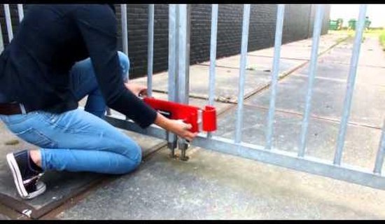 Persoon in blauwe jeans monteert een rood DoubleLock containerslot op een hek.